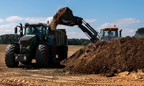 farm tractor in field having trailer filled with dirt by front end loader machine. Biosolids testing, Biosolids regulations, Biosolids disposal, Land application of biosolids
