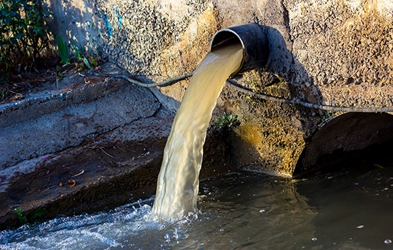 pipe sticking out of cement wall draining murky water into holding pond. Wastewater monitoring, Wastewater sampling, Stormwater testing, Wastewater surveillance