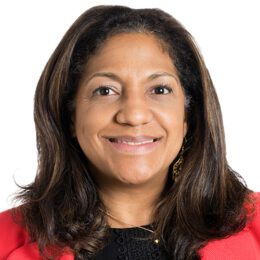 Portrait of a smiling woman with shoulder-length dark hair wearing a red blazer against a white background.