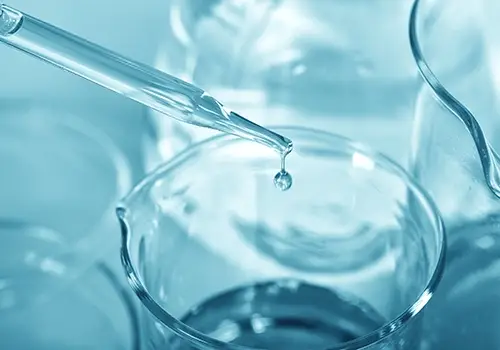 Pipette releasing a droplet into a glass beaker in a laboratory setting.