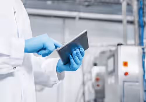 Scientist in a white lab coat and blue gloves using a tablet in a sterile laboratory.