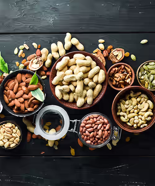 Assorted nuts in bowls on a dark wooden table, including almonds, cashews, pistachios, walnuts, and hazelnuts.