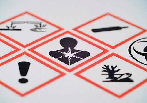 Close-up of red diamond hazard signs on a label, showing an exclamation mark, biohazard-like symbol, and other warning icons in a grid.