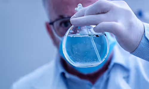 Scientist working in laboratory holding beaker with gloved hand containing water with microplastics. Pace® UCMR testing services. UCMR 6.