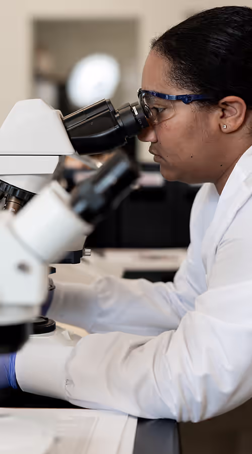 Female Pace® scientist wearing goggles and gloves examines samples using a compound microscope in a laboratory.