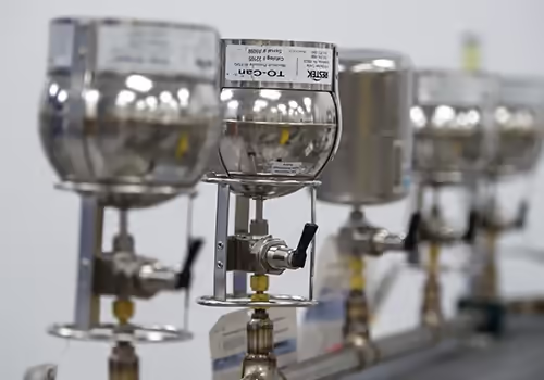 Row of stainless steel gas regulators attached to a pressure manifold in a lab, with each regulator connected to tubing and fittings